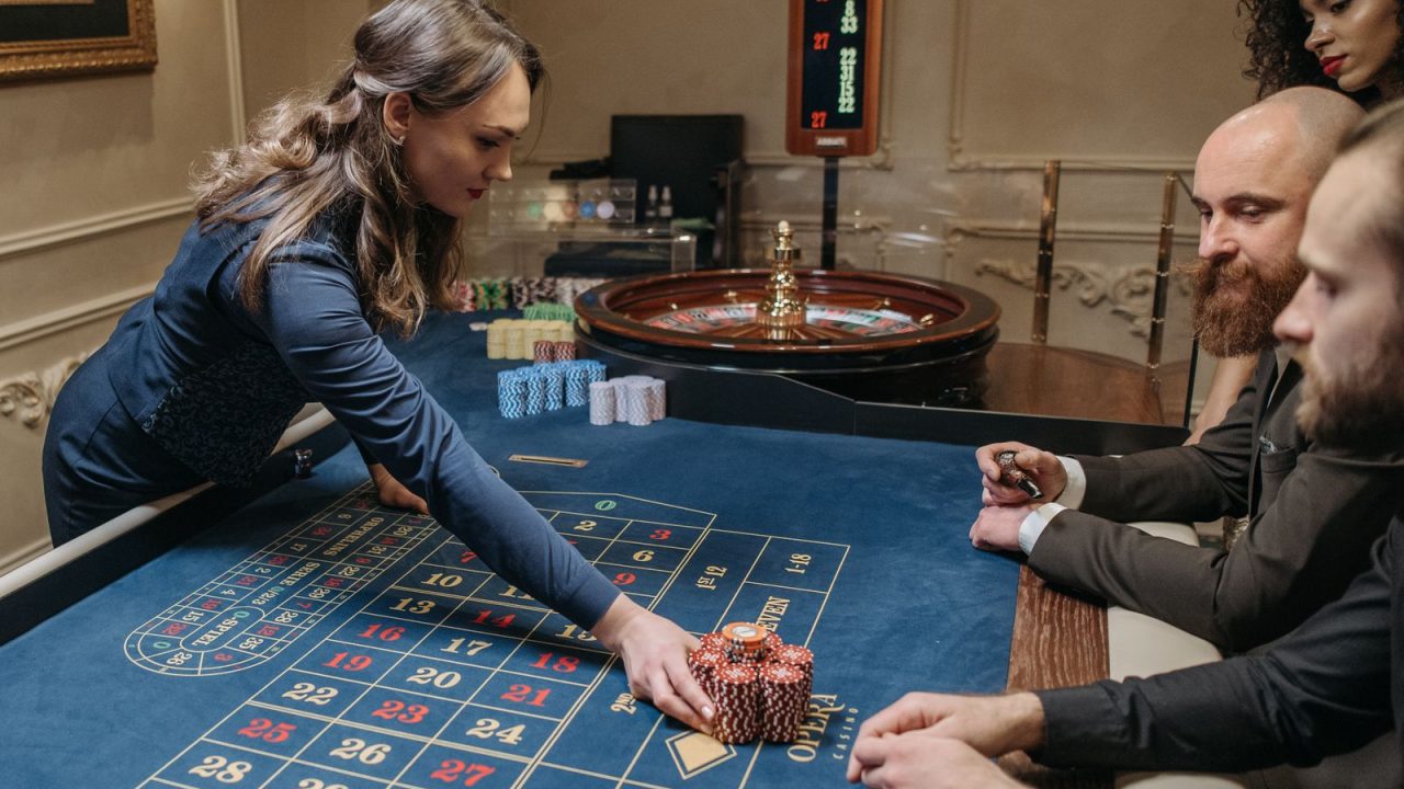 A group of people playing roulette at a casino with a female dealer organizing chips on the table.